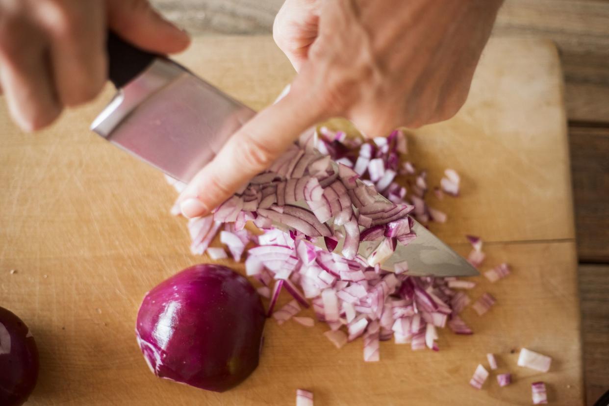 Spanish onion chopped using sharp kitchen knife. Close up, selective focus, unrecognizable person. chopped particles removed from blade with finger