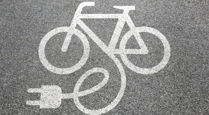 An image of a bike painted in white on asphalt with an electric cord drawn as coming out of the frame.