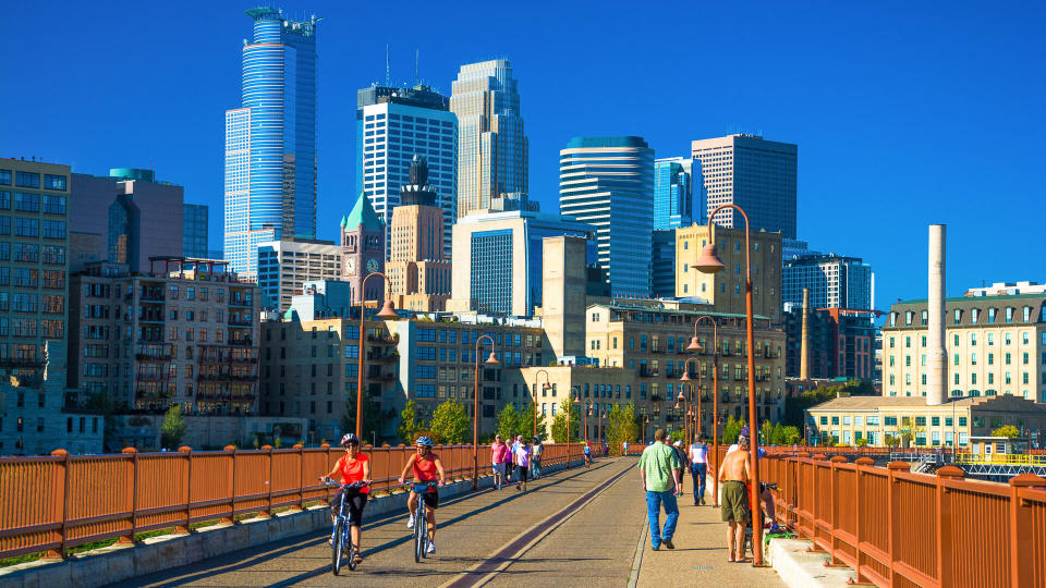 Active people walking and biking on the Stone Arch Bridge during a nice sunny day with the Downtown Minneapolis skyline in the background.