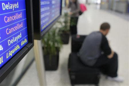 A passenger waits under a flight status board showing delayed and cancelled JetBlue flights at Logan International Airport in Boston, Massachusetts January 6, 2014. REUTERS/Brian Snyder