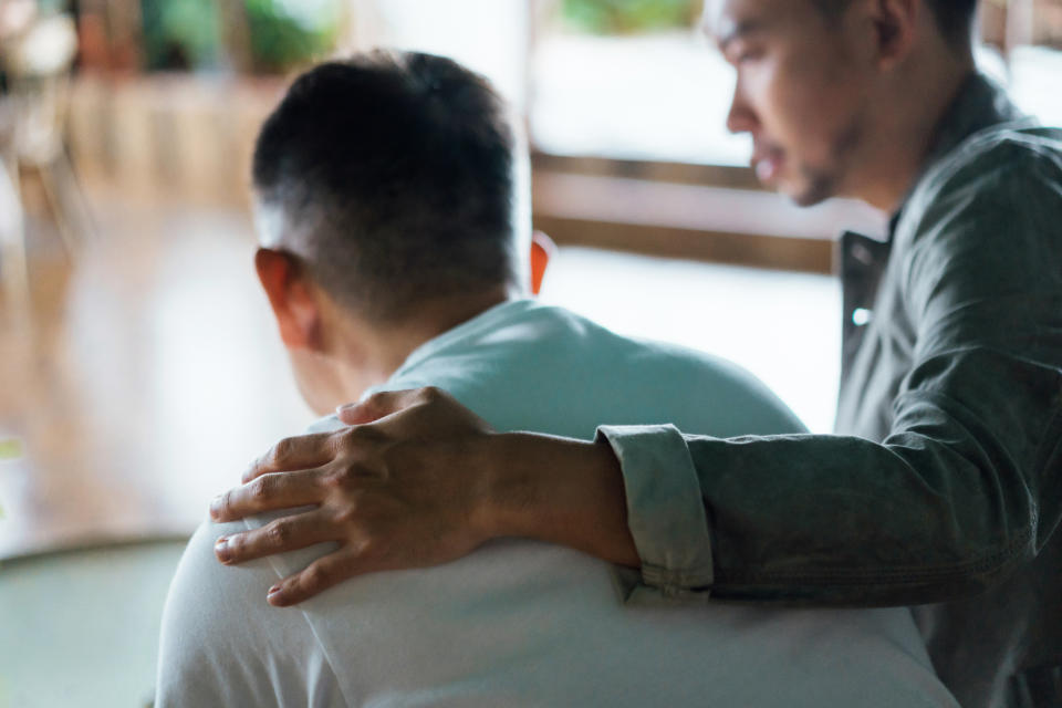 Two unidentified people, one with a hand on the other's shoulder, appearing to provide comfort