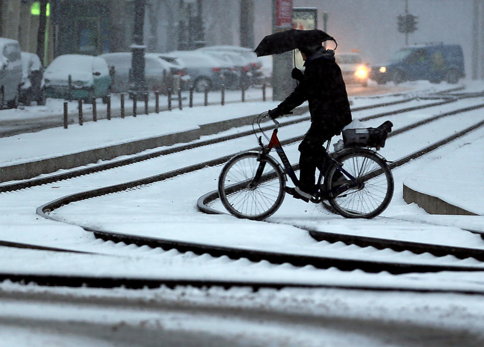 A cyclist holds an umbrella as he crosses tracks during snowfalls in Cologne, Germany, Tuesday, March 12, 2013. Fresh snow fell in wide oparts of Germany. (AP Photo/dpa, Oliver Berg)