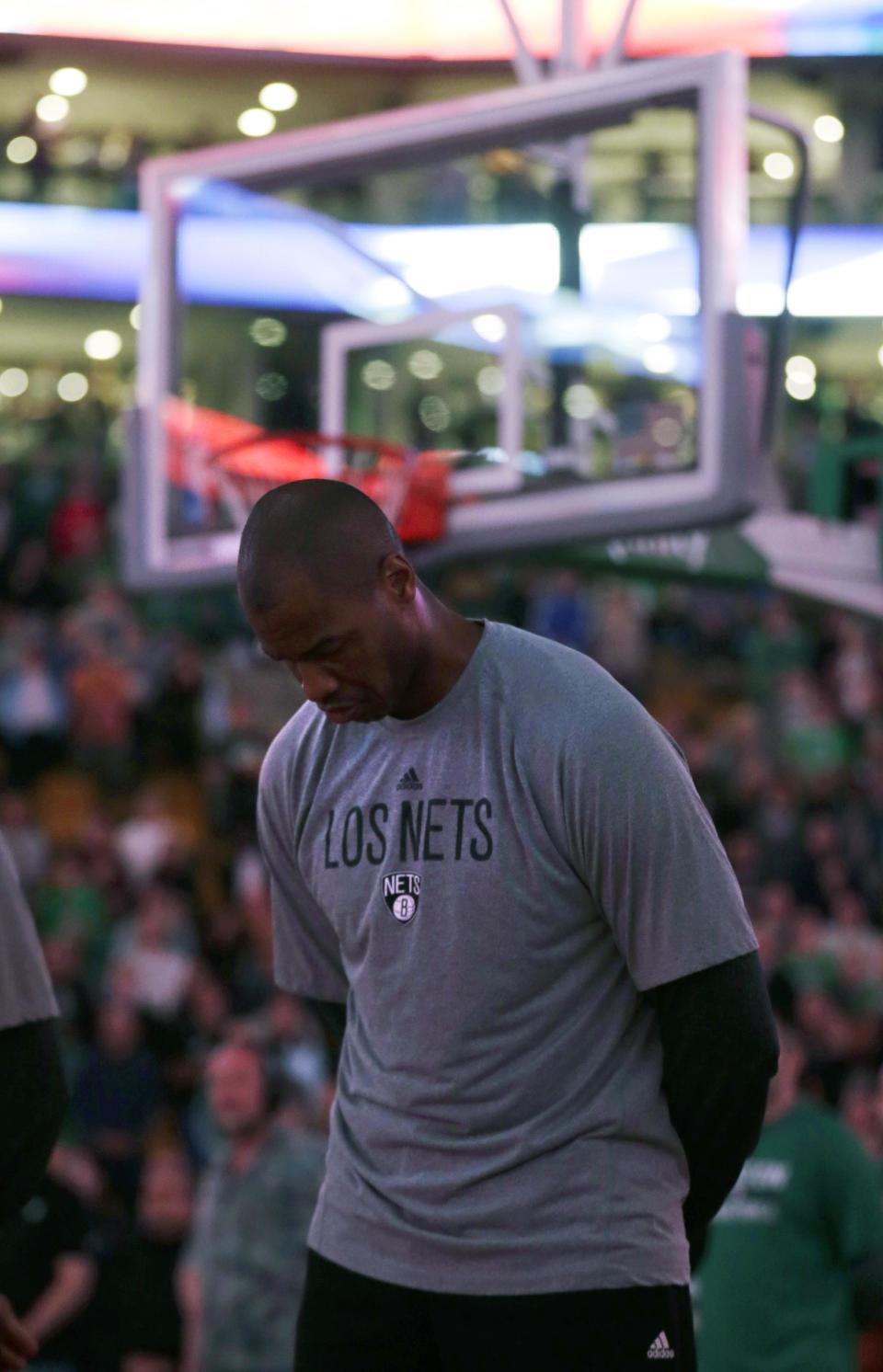 With the stadium lights dimmed, Brooklyn Nets center Jason Collins listens to the national anthem before the Nets faced the Boston Celtics in an NBA basketball game, Friday, March 7, 2014, in Boston. (AP Photo/Charles Krupa)