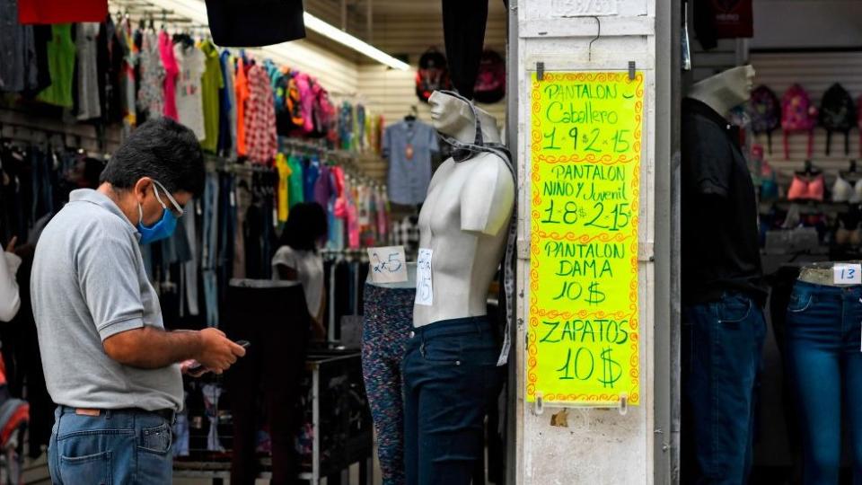 Un hombre, junto a un cartel con pecios en dólares en un comercio de Caracas.