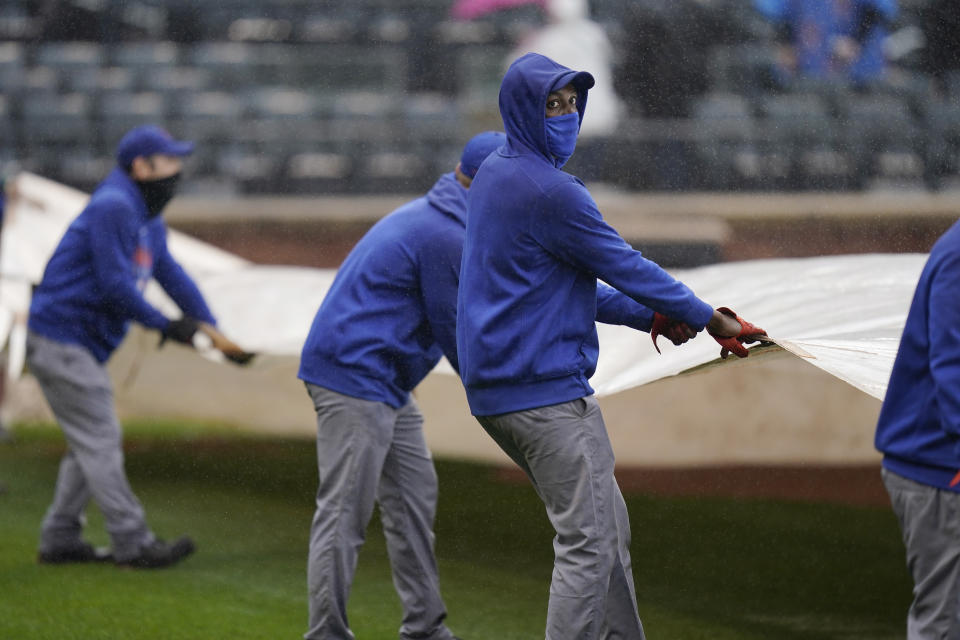 New York Mets employees put a tarp over the field during a delay in the first inning of a baseball game against the Miami Marlins at Citi Field, Sunday, April 11, 2021, in New York. The game was delayed at the top of the first inning due to rain. (AP Photo/Seth Wenig)