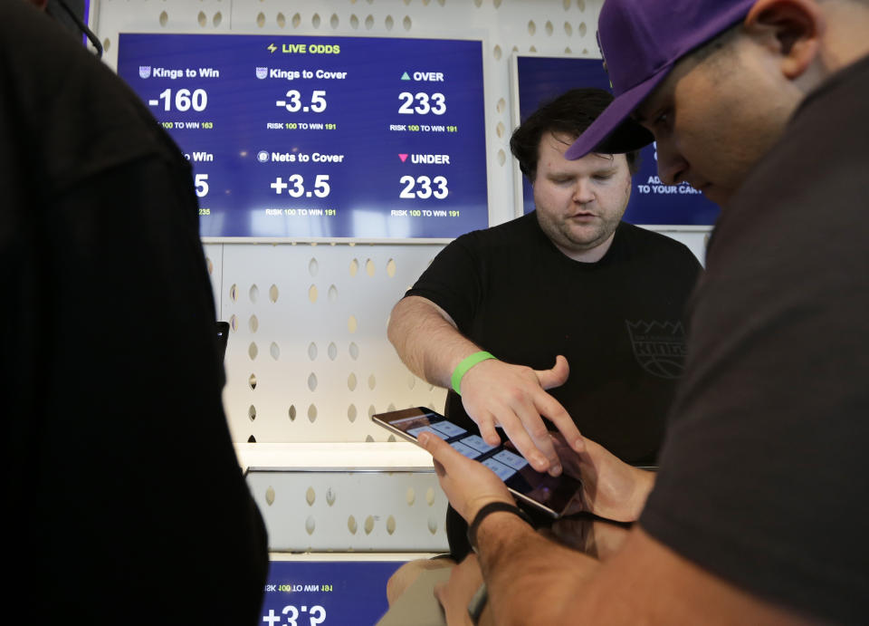 FILE - In this March 19, 2019, file photo, Zack Shelton, left, of Swish Analytics, explains how to place a bet at the Skyloft Predictive Gaming Lounge inside the Golden 1 Center, home of the NBA's Sacramento Kings, in Sacramento, Calif. Professional sports leagues have found a way to cash in by selling their official data to gambling companies, making the case that the leagues are creating new products for gamblers to bet on. (AP Photo/Rich Pedroncelli, File)