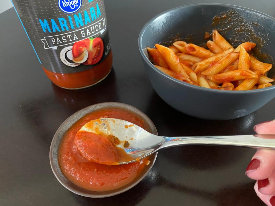 spoon showing close-up of kroger pasta sauce with a bowl of pasta in the background