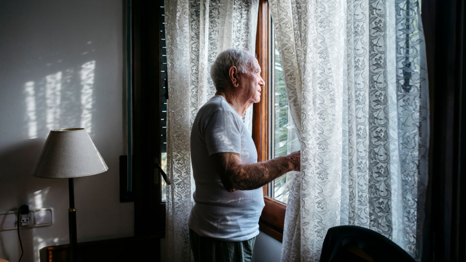 An elderly man looking out a window in his home to represent older Aussies taking on flatmates.