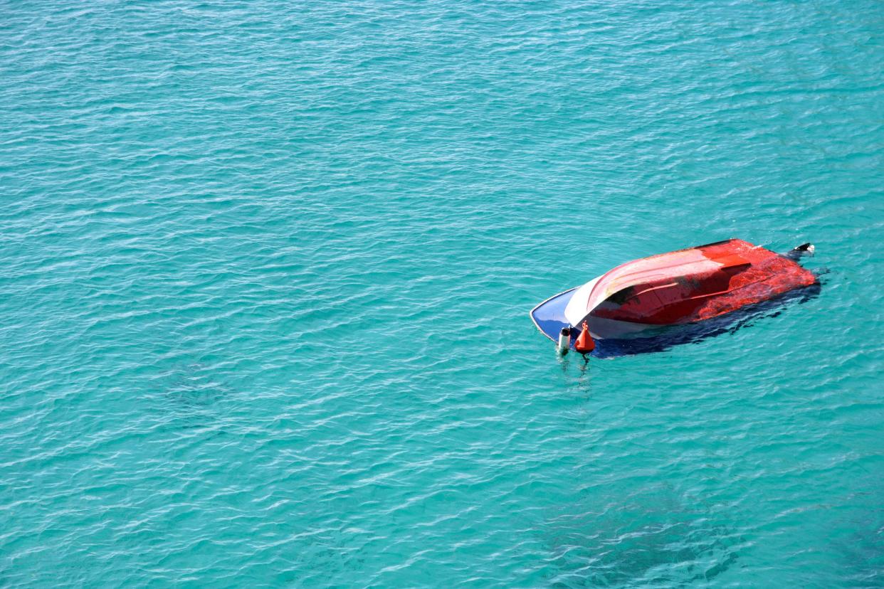 A boat capsized (overturned) in the middle of the sea. Copy space on left.
