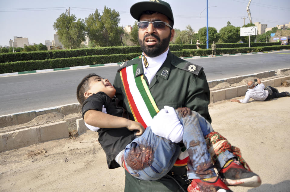 In this photo provided by the Iranian Students' News Agency, ISNA, a Revolutionary Guard member carries a wounded boy after a shooting during a military parade marking the 38th anniversary of Iraq's 1980 invasion of Iran, in the southwestern city of Ahvaz, Iran, Saturday, Sept. 22, 2018. Gunmen attacked the military parade, killing at least eight members of the elite Revolutionary Guard and wounding 20 others, state media said. (Behrad Ghasemi/ISNA via AP)