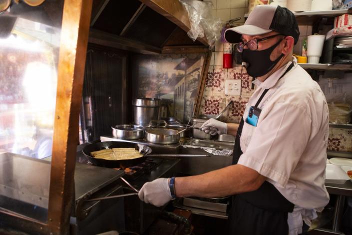 Edward Flores, wearing a mask, holds tongs while cooking at a stovetop in his restaurant