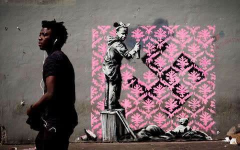 A man walks past a recent artwork by street artist Banksy in Paris  - Credit: AFP