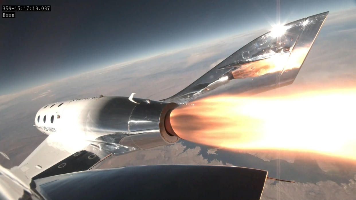  A silver-white space plane fires its rocket engine with the curve of earth and the blackness of space in the background. 