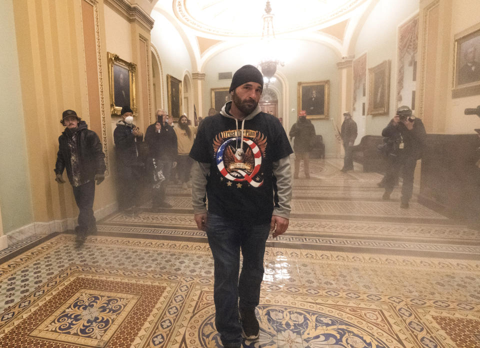 FILE - Smoke fills the walkway outside the Senate Chamber as supporters of President Donald Trump, including Doug Jensen, center, are confronted by U.S. Capitol Police officers, Jan. 6, 2021, inside the Capitol in Washington. A trial is set to open for Jensen, who ran after a police officer retreating up a flight of stairs during a mob's attack on the U.S. Capitol, a harrowing encounter captured on video. Jensen, who wore a shirt promoting the QAnon conspiracy theory, told the FBI that he wanted to be a "poster boy" for the events that unfolded on Jan. 6, 2021. (AP Photo/Manuel Balce Ceneta, File)