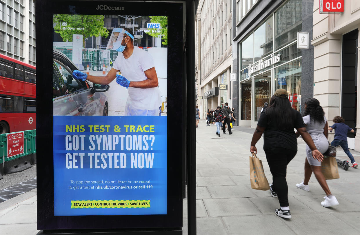 Shoppers walk past a screen on a bus stop displaying a NHS notice on test and trace on Oxford Street, London, as non-essential shops in England open their doors to customers for the first time since coronavirus lockdown restrictions were imposed in March. Picture date: Monday June 15, 2020.