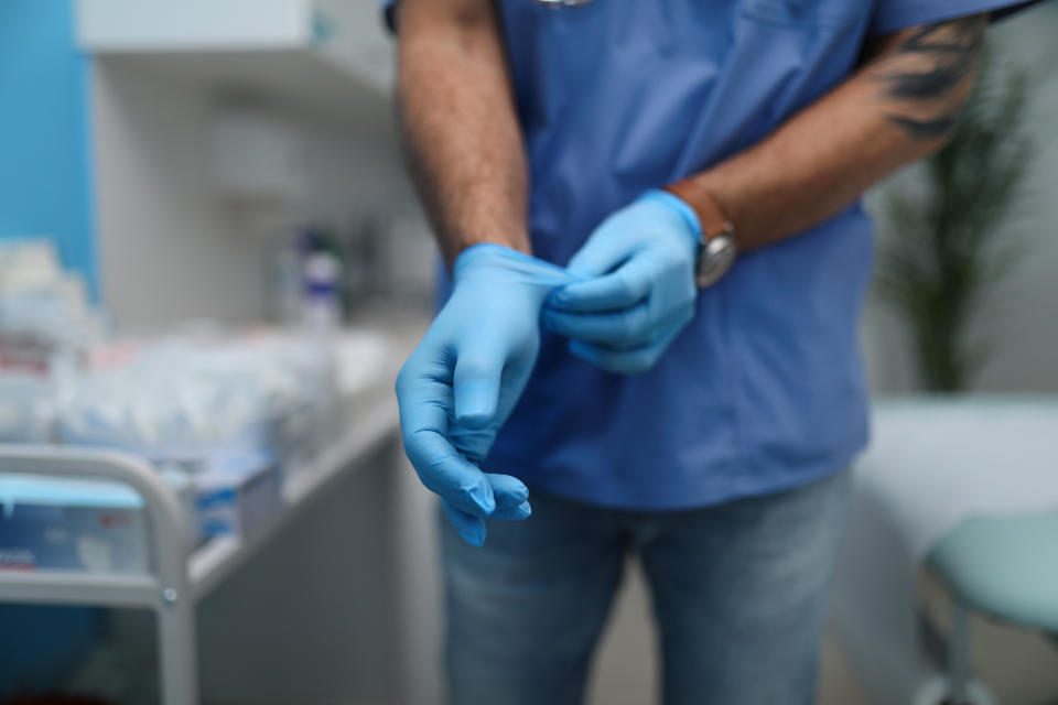 Cut out of male doctor putting on protective blue gloves.