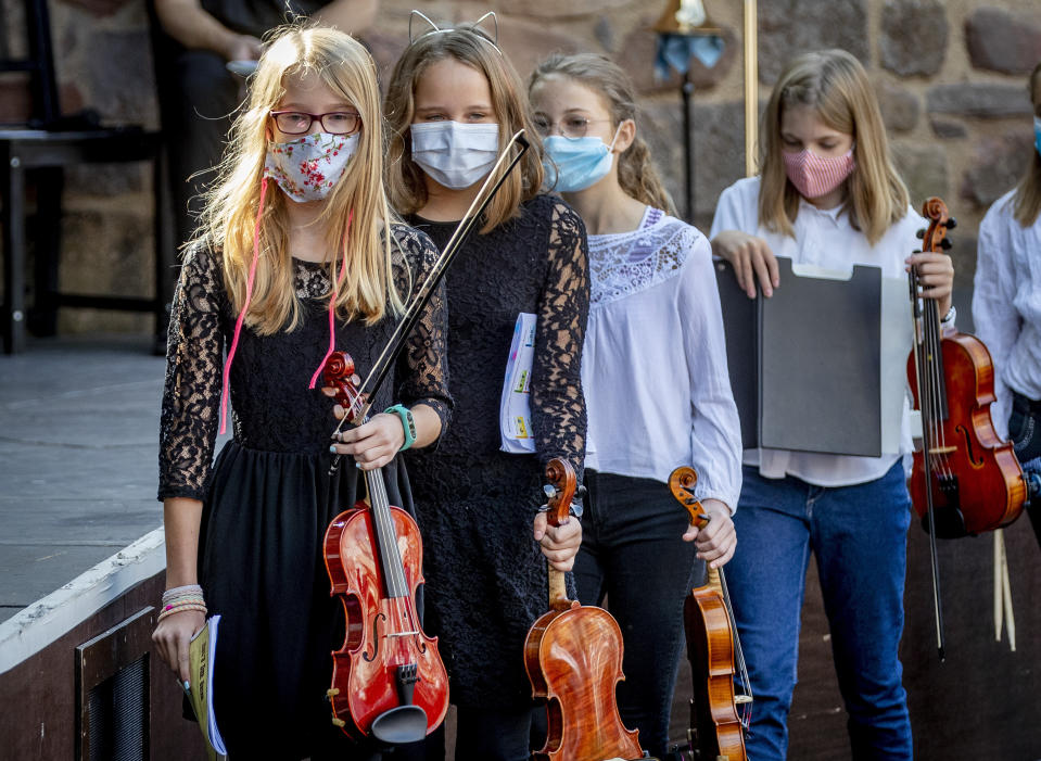 Young violinists wear face masks on the way to their music school concert in the old castle in Bad Vilbel near Frankfurt, Germany, Sunday, Sept. 20, 2020. (AP Photo/Michael Probst)