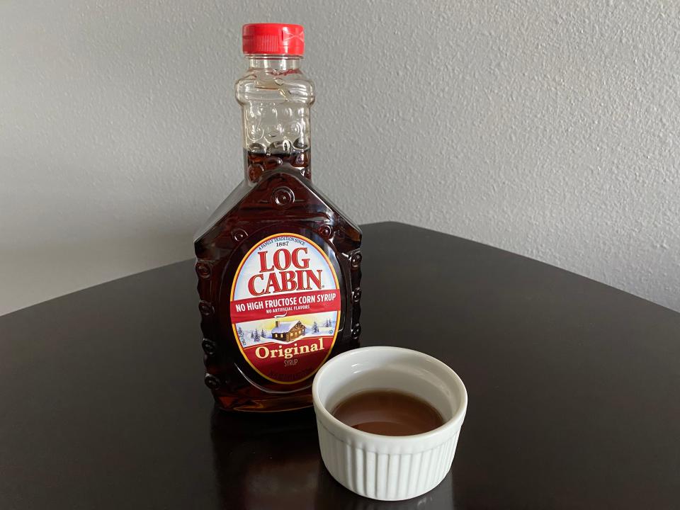 bottle of log cabin syrup next to a white ramekin filled with the syrup
