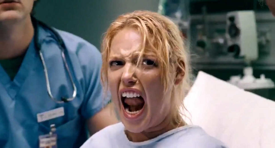 Katherine Heigl in Knocked Up, wearing a hospital gown, screams in a medical setting with doctors in blue scrubs nearby