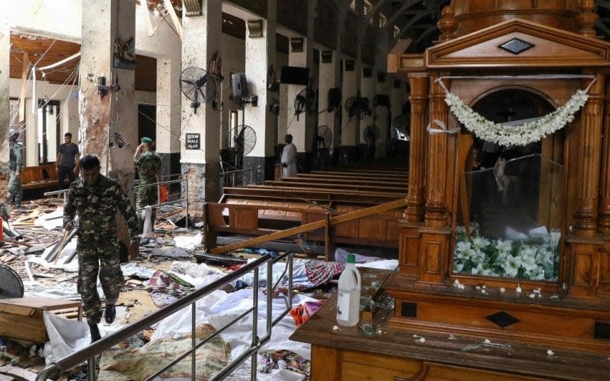 Sri Lankan security personnel walk past dead bodies covered with blankets amid blast debris at St. Anthony's Shrine following an explosion in the church in Kochchikade in Colombo - AFP or licensors