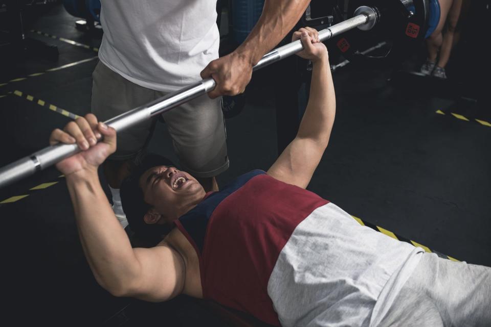 a young man doing bench presses powers on through one last rep while another guy spots him chest workout at the gym