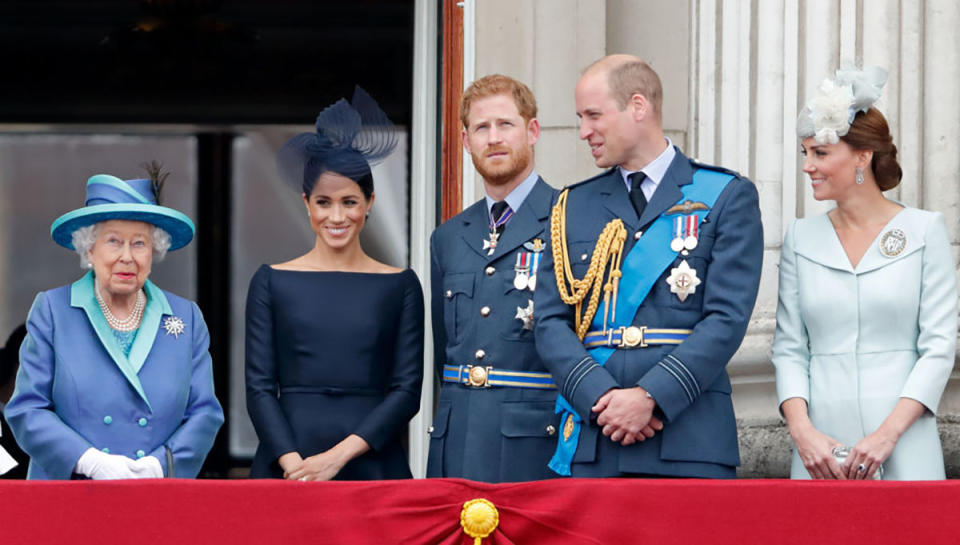 The Queen in a blue outfit and hat, Meghan Markle in a black outfit and hat, Prince Harry and William in jackets with medals attached and Kate in a pale blue outfit and hat stand on Buckingham's Palace balcony