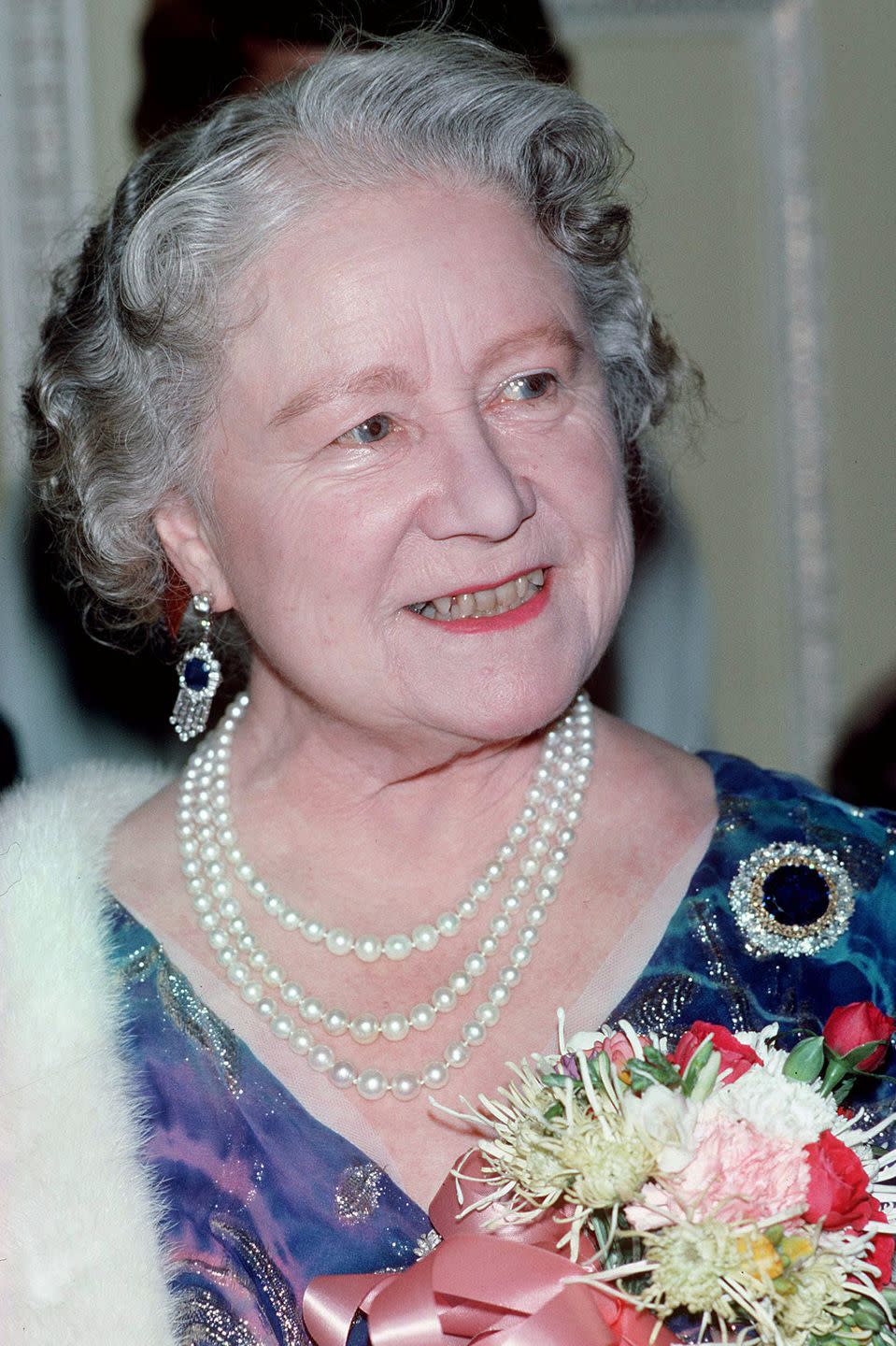 <p>The Queen Mother is pictured here in 1986 wearing her beloved Russian Sapphire Cluster Brooch with a pair of sapphire and diamond fringe earrings.</p>