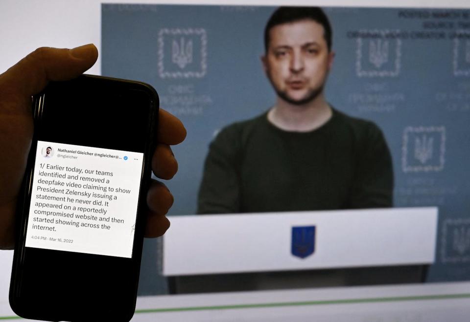 a hand holds a smartphone with text on it in front of a screen with a man in front of a lectern