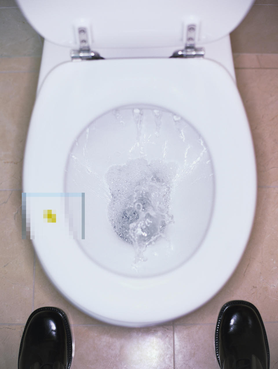 Overhead view of a flushing toilet with shoes visible at the bottom of the image