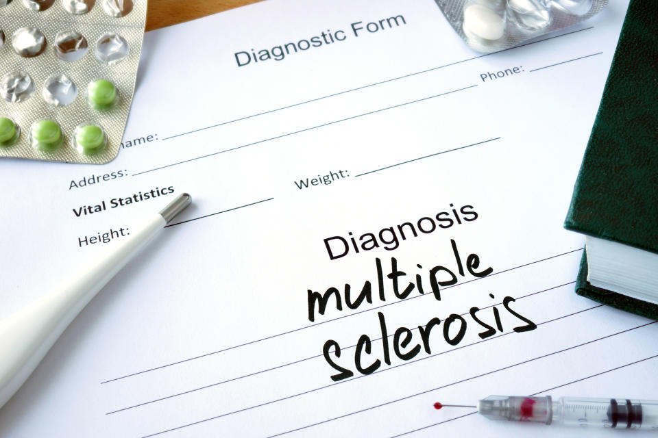 Multiple sclerosis written on a diagnosis form with book, medication and a thermometer