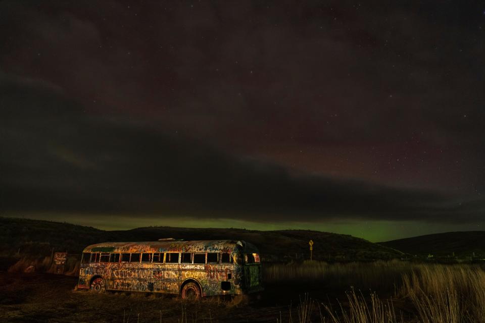 An aurora borealis, also known as the northern lights, is seen in the night sky as clouds move in above a roadside landmark known as "That NW Bus" in the early morning hours of Monday, Feb. 27, 2023, in Washtucna, Wash.