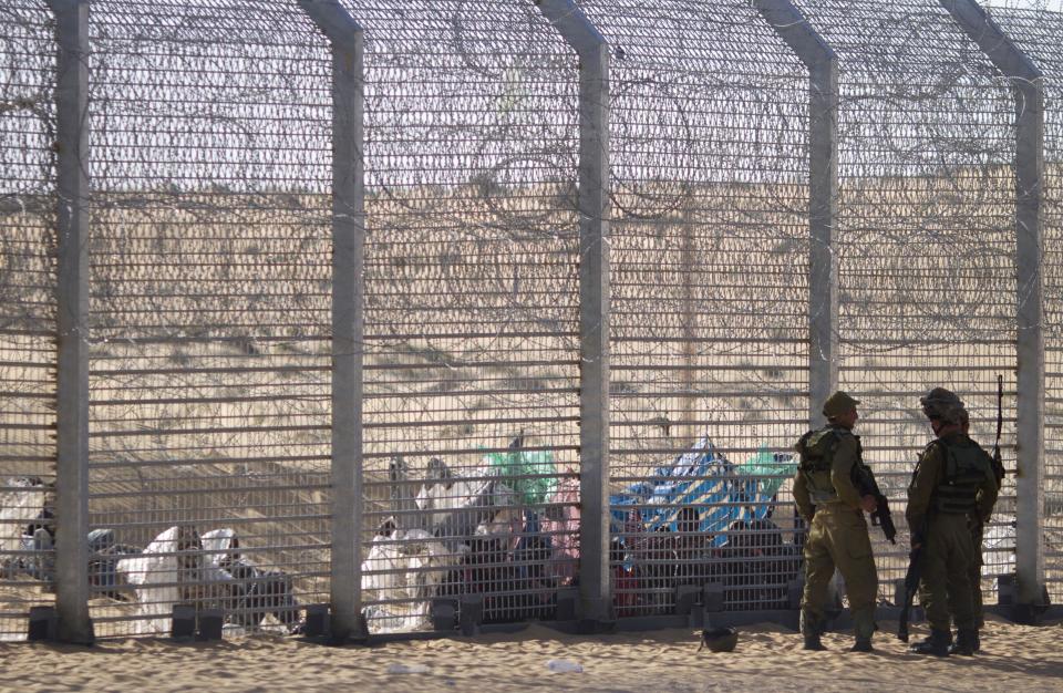 African refugees sit on the ground behind a border fence after they attempted to cross illegally from Egypt into Israel as Israeli soldiers stand guard near the border with Egypt, in southern Israel, Tuesday, Sept. 4, 2012. Israel is staunching the flow of African migrants who have poured into the Jewish state by the tens of thousands, rapidly building a border fence and implementing a new policy of detaining Africans upon arrival. Israel’s army says over the past few days, a group of African migrants has waited on the Egyptian side of the fence. Israeli soldiers are providing the group with water, but not allowing them into Israel.(AP Photo/Ariel Schalit)