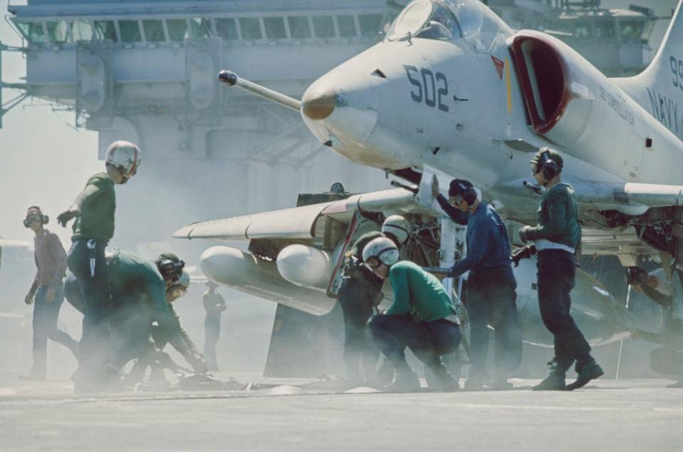 United States Navy personnel shrouded in steam as they prepare a Douglas A-4 Skyhawk for take-off from USS Constellation, a Kitty Hawk-class supercarrier, off the coast of South Vietnam, 16th August 1966