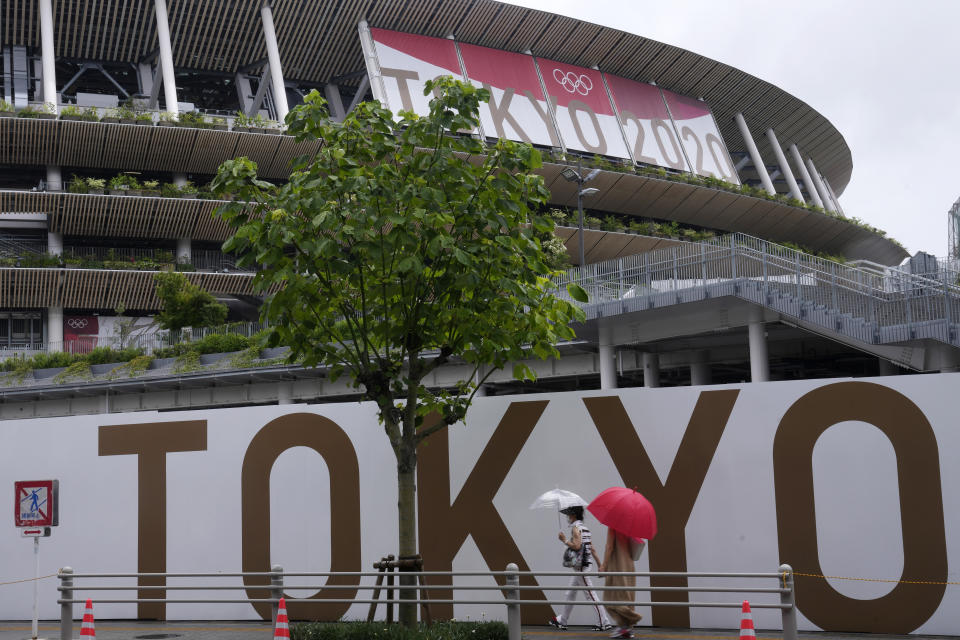 FILE - In this July 27, 2021, file photo, people walk past the National Stadium in Tokyo. The price tag for the Tokyo Olympics is $15.4 billion. Tokyo built eight new venues. The two most expensive were the National Stadium, which cost $1.43 billion, and the new aquatic center, priced a $520 million. (AP Photo/Kiichiro Sato, File)