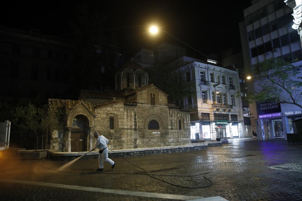 In this Thursday, April 2, 2020 photo, a municipal worker wearing a protective suit sprays disinfectant in front of the Kapnikarea Orthodox church in central Athens during the lockdown. Deserted squares, padlocked parks, empty avenues where cars were once jammed bumper-to-bumper in heavy traffic. The Greek capital, like so many cities across the world, has seen its streets empty as part of a lockdown designed to stem the spread of the new coronavirus. (AP Photo/Thanassis Stavrakis)