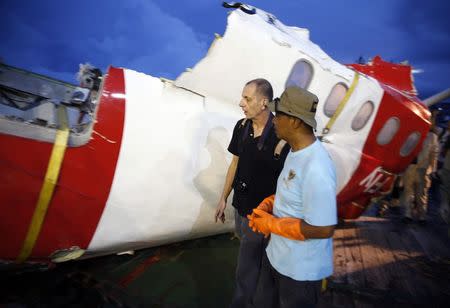 Investigators walk near a section of the tail of AirAsia Flight QZ8501 passenger plane in Kumai Port, near Pangkalan Bun, Central Kalimantan January 11, 2015. REUTERS/Darren Whiteside