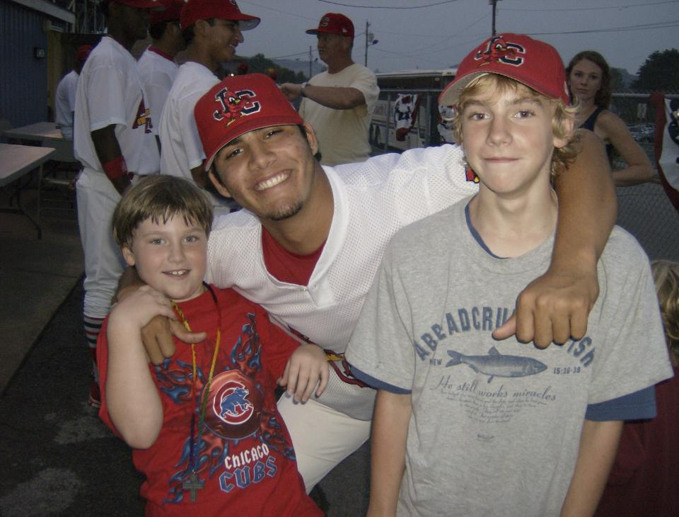 This photo provided by TeriAnn Reynolds shows her children, Garrett, left, and Matthew Reynolds posed with minor league baseball player Reynier Gonzalez at a baseball game in Johnson City, Tenn., in July 2007. TeriAnn Reynolds and her family were part of a little-known but vital piece of baseball's minor leagues for decades: host families. Host family programs were suspended during the coronavirus pandemic over health concerns. Now, they may never return. (Photo courtesy TeriAnn Reynolds via AP)