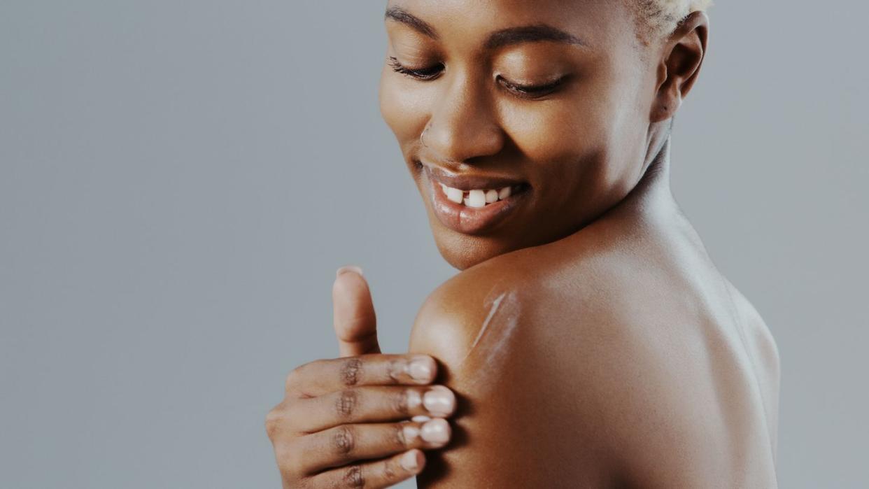 applying lotion to her shoulder against a gray studio background