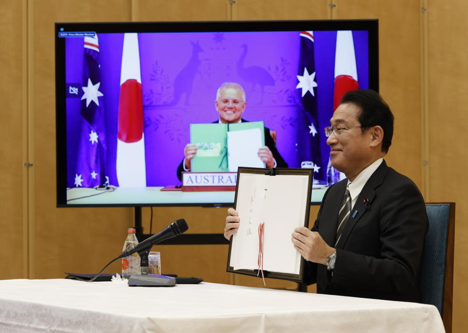 Japan's Prime Minister Fumio Kishida, right, and Australia's Prime Minister Scott Morrison, seen on screen, show off signed documents during a virtual summit to sign the Reciprocal Access Agreement, at Kishida's official residence in Tokyo, Japan Thursday, Jan. 6, 2022. The leaders of Japan and Australia signed a “landmark” defense agreement Thursday that allows closer cooperation between their militaries and stands as a rebuke to China's growing assertiveness in the Indo-Pacific region. (Issei Kato/Pool Photo via AP)