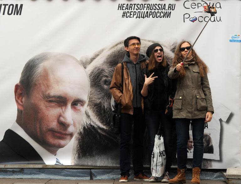 People pose for a selfie photograph in front of a banner depicting Russian President Vladimir Putin in St. Petersburg on May 2, 2015