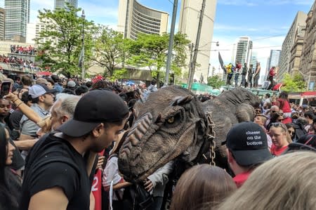 A fan dressed as a dinosaur walks through the crowd as Toronto fans fill the streets in front of city hall during the Toronto Raptors NBA Championship celebration parade at Nathan Phillips Square in Toronto