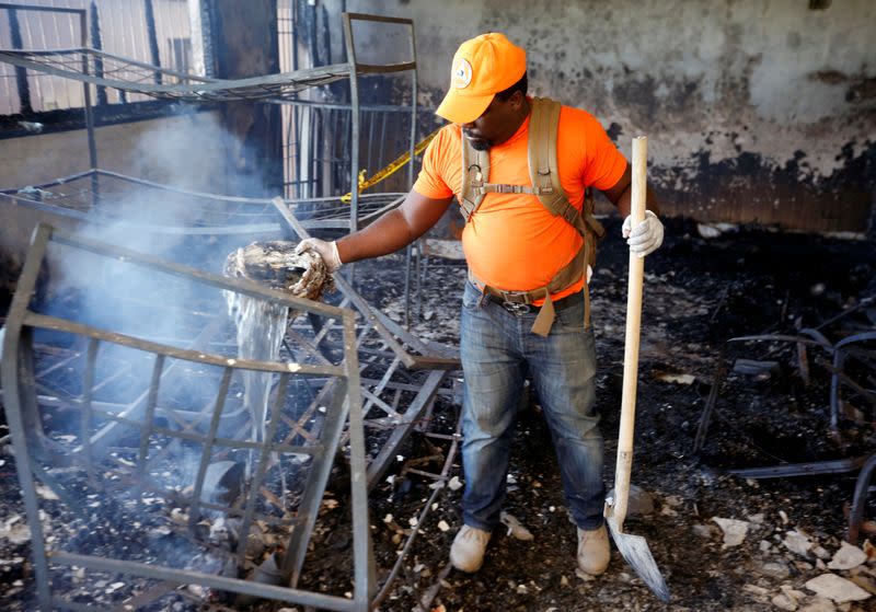 A civil protection worker pours water over burning debris inside a bedroom at an orphanage after it was destroyed in a fire, in Port-au-Prince