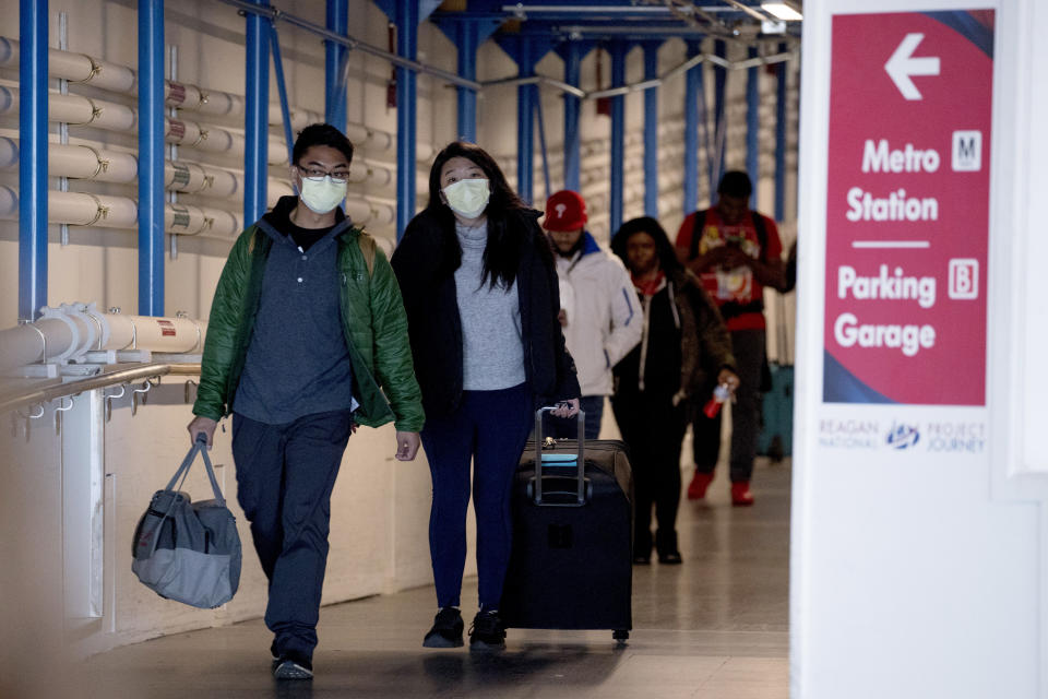 People wearing a masks walk through a terminal at Ronald Reagan Washington National Airport, Monday, March 16, 2020, in Arlington, Va. (AP Photo/Andrew Harnik)