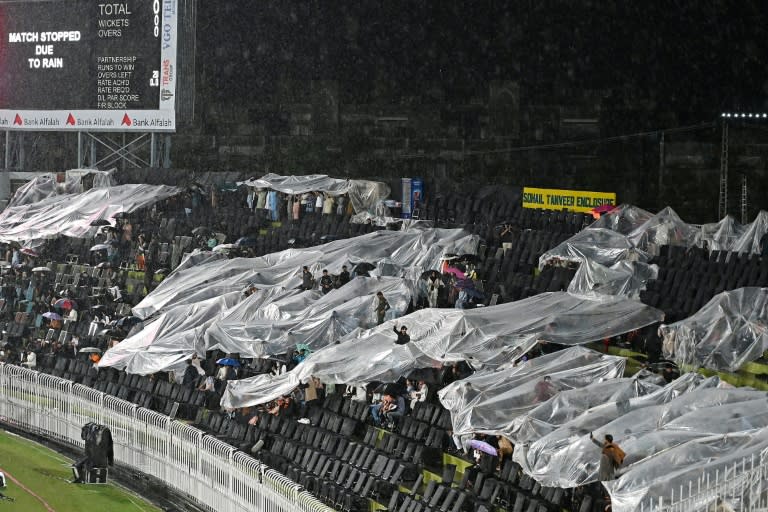 Rain pain: Spectators sit under plastic sheets in the stands (Aamir QURESHI)