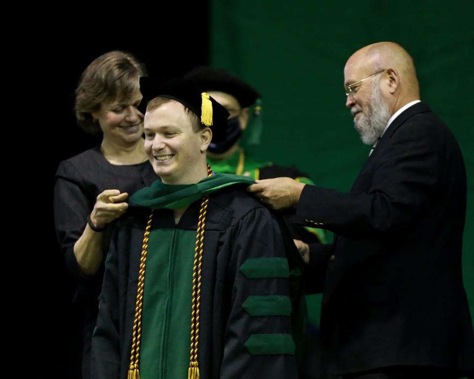 Dr.s Amy and Don Givler of Tyler, Texas, hood their son, Dr. John Givler, Saturday, May 15, during 2021 Arkansas College of Health Education Commencement Ceremony at UAFS’ Stubblefield Center. 