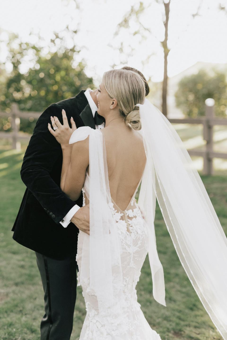 A bride hugs her groom, showing off her backless wedding dress.