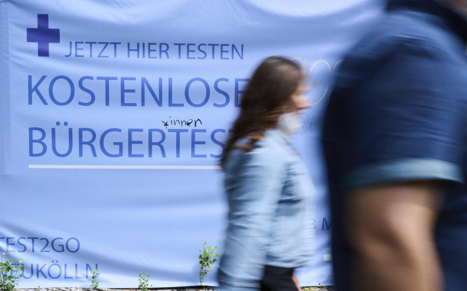 'Free citizen testing' is written on a poster as people walk by at a Corona teste center in Berlin, Germany, Tuesday, Aug. 9, 2021. The heads of government of the federal states consult with Chancellor Merkel on Aug. 10, 2021 about the further handling of Corona vaccinations and tests. (Annette Riedl/dpa via AP)