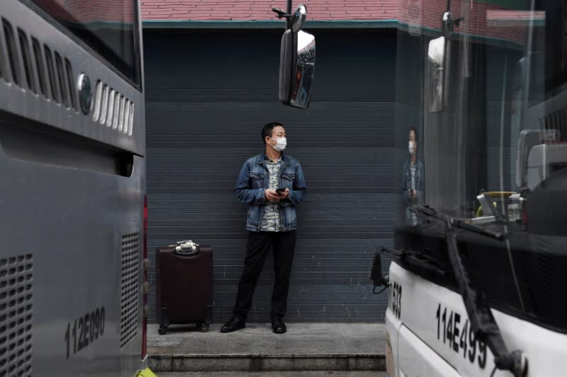 A man wearing a protective mask stands next to a suitcase at a bus terminal in Wuhan