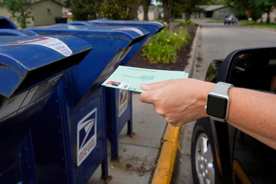 A voter puts a ballot in a mailbox.