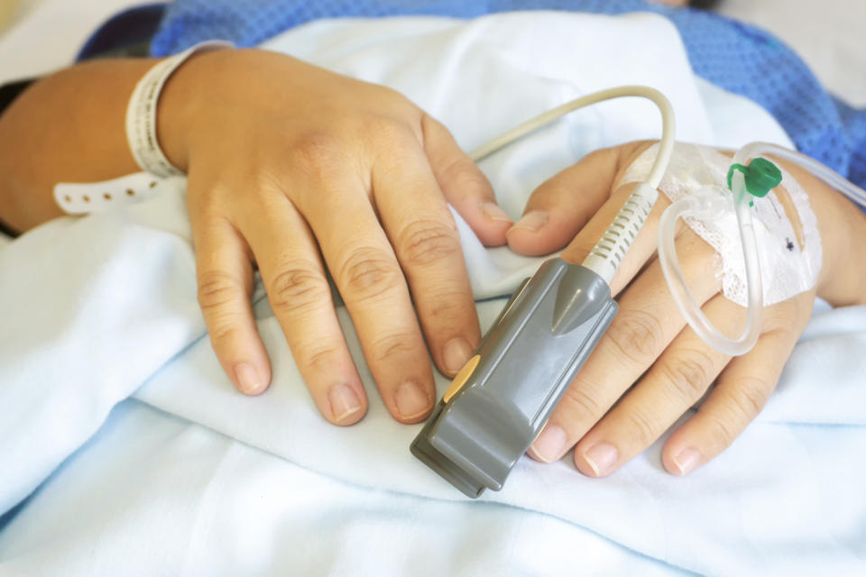 A patient's hand with a pulse oximeter attached, resting on a hospital bed